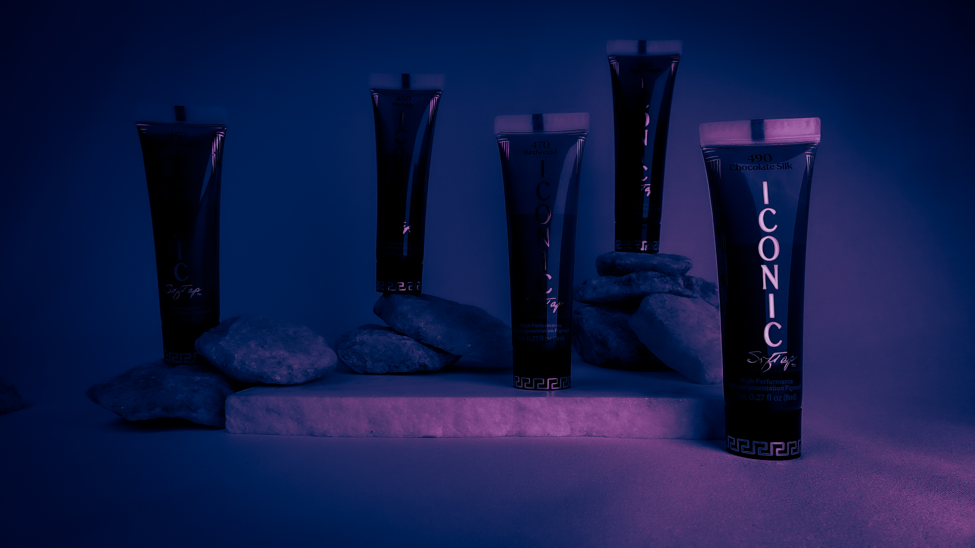 Five dark blue tubes with 'Iconic' branding on a stone surface against a dark background