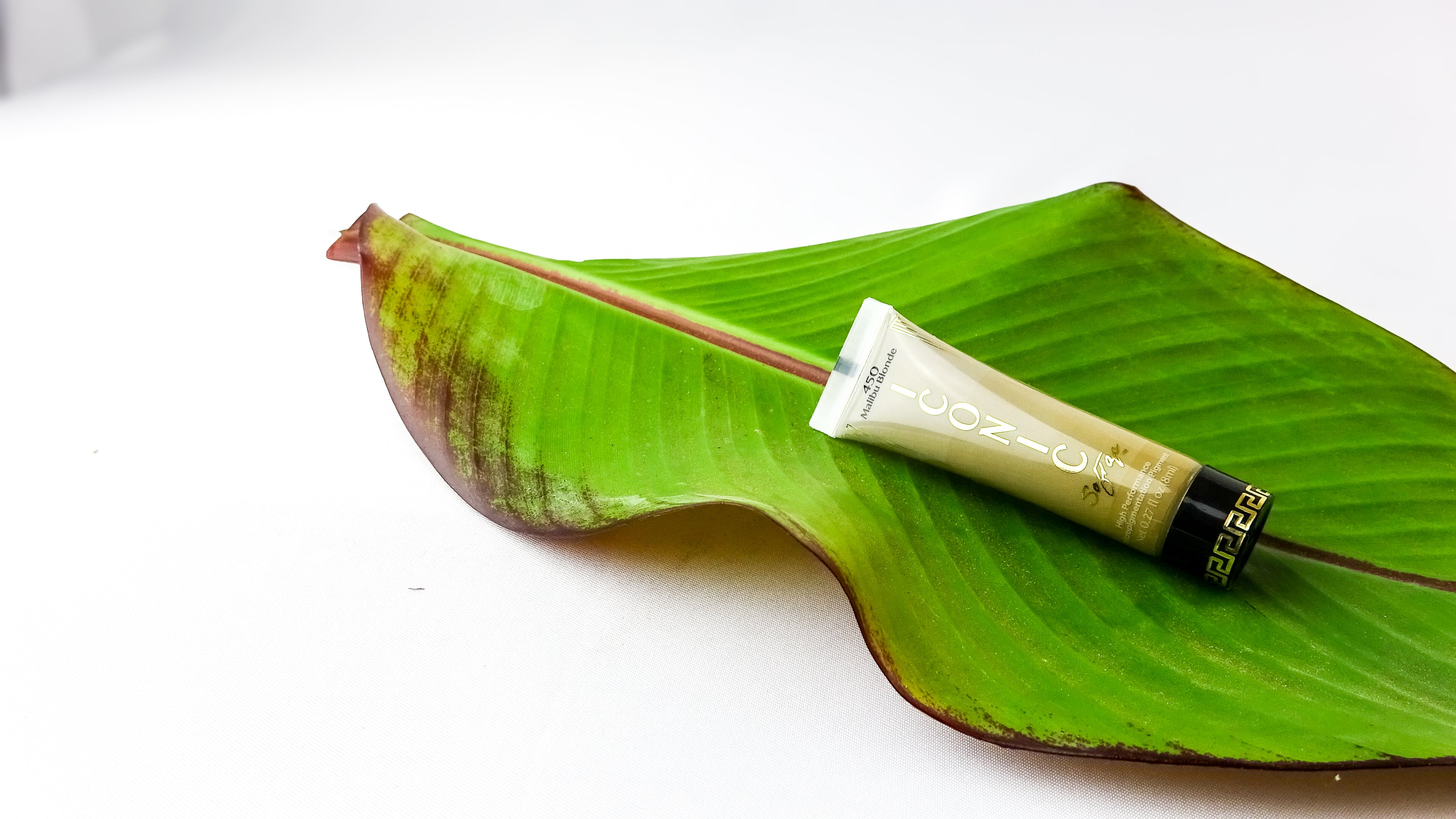 Tube of Blonde colored Permanent makeup pigment cream on a large green leaf with a white background