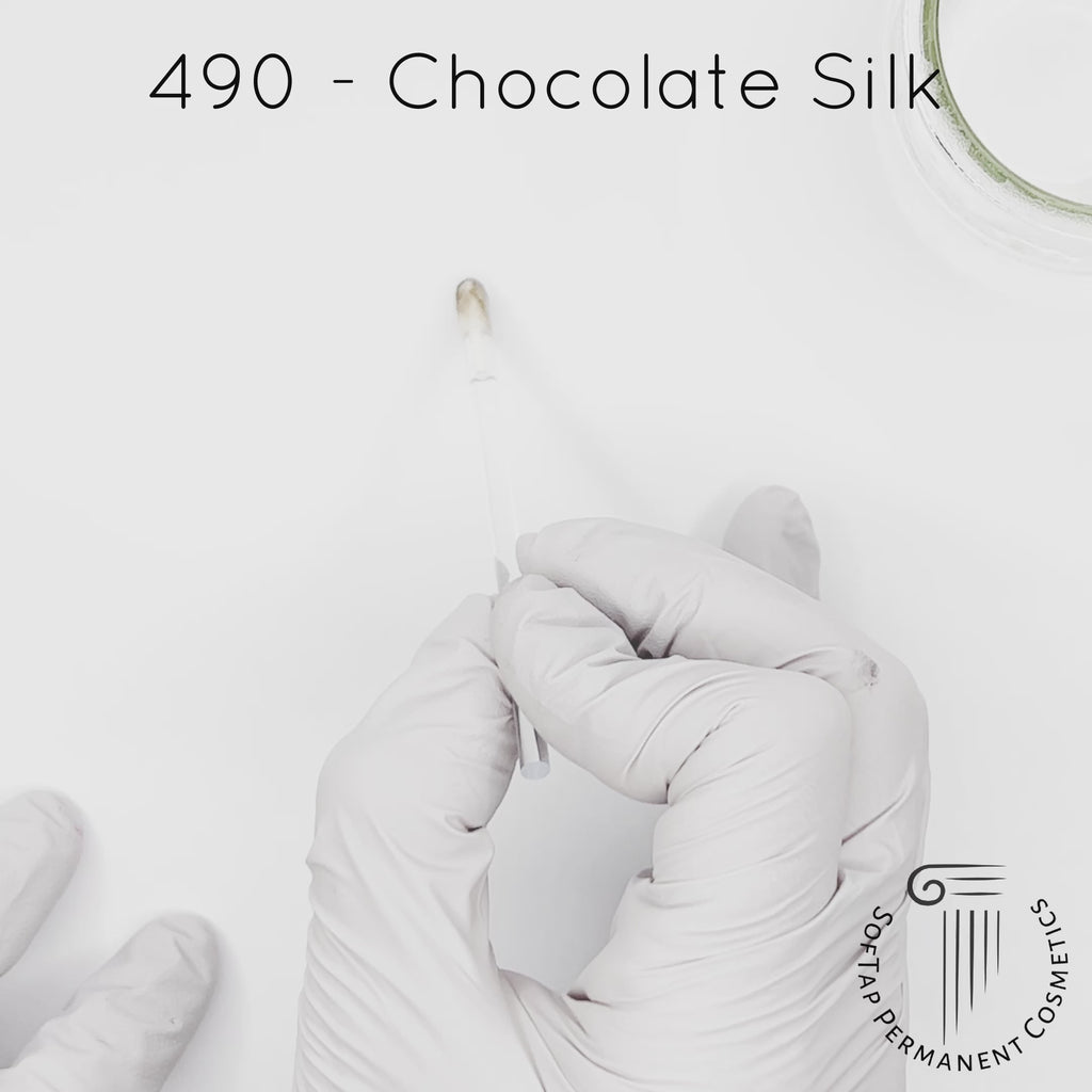 white gloved hand with white brush smearing SofTap dark brown Chocolate Silk Color for permanent eyebrows