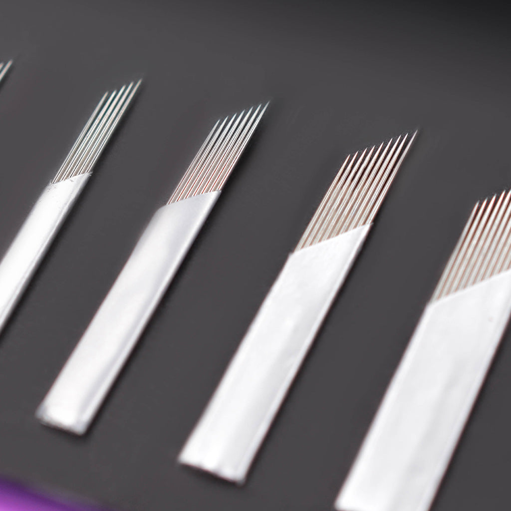 Close-up of several SofTap permanent makeup foil cartridge needles arranged diagonally on a dark gray background.
