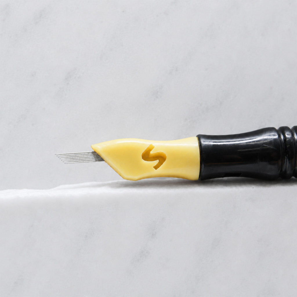 A close-up of SofTap 10 fine pmu needle click tip, resting on a white marble surface.
