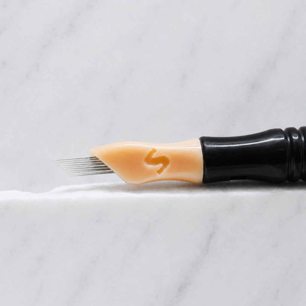 A close-up of SofTap 11 ultimate pmu needle click tip, resting on a white marble surface.