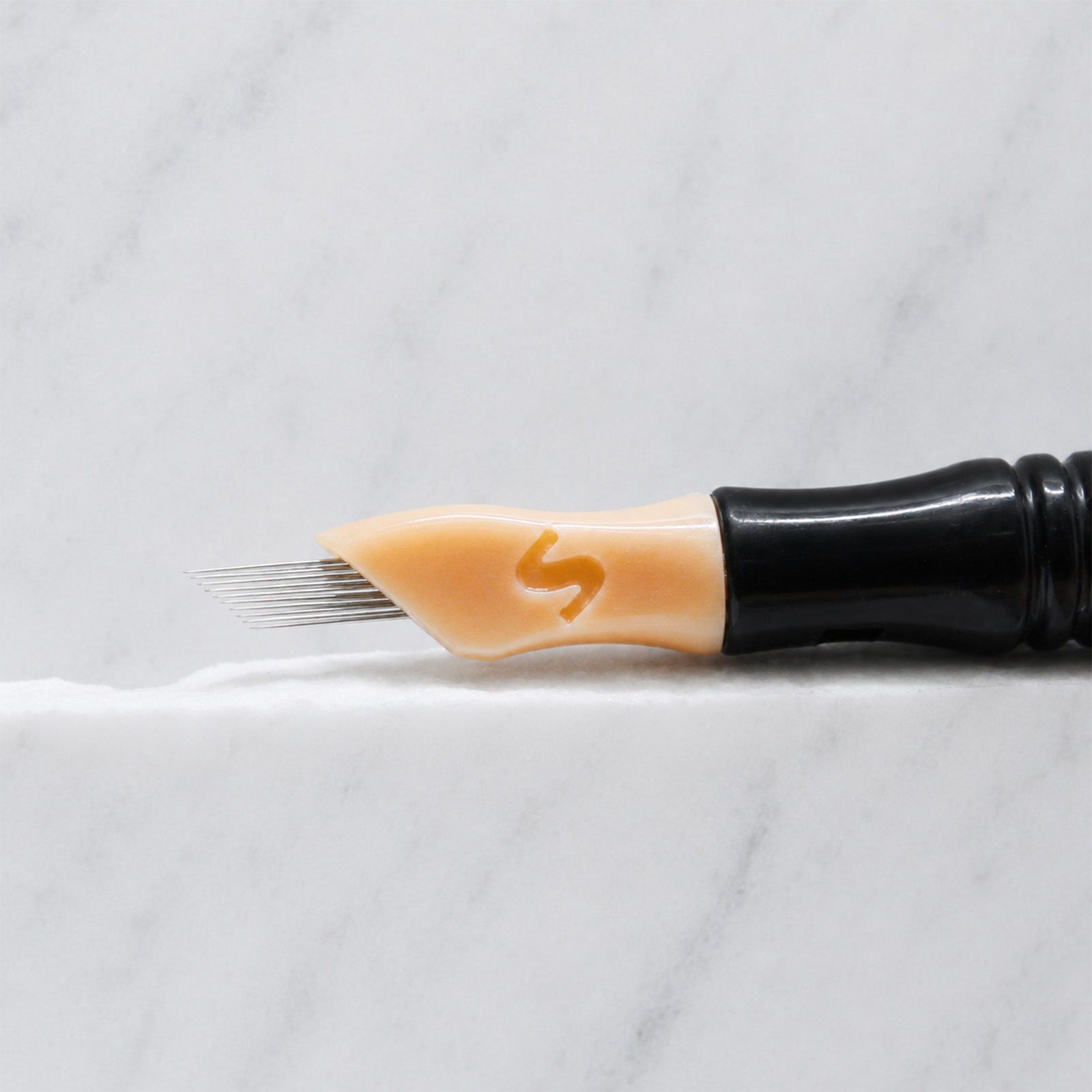 A close-up of SofTap 11 ultimate pmu needle click tip, resting on a white marble surface.