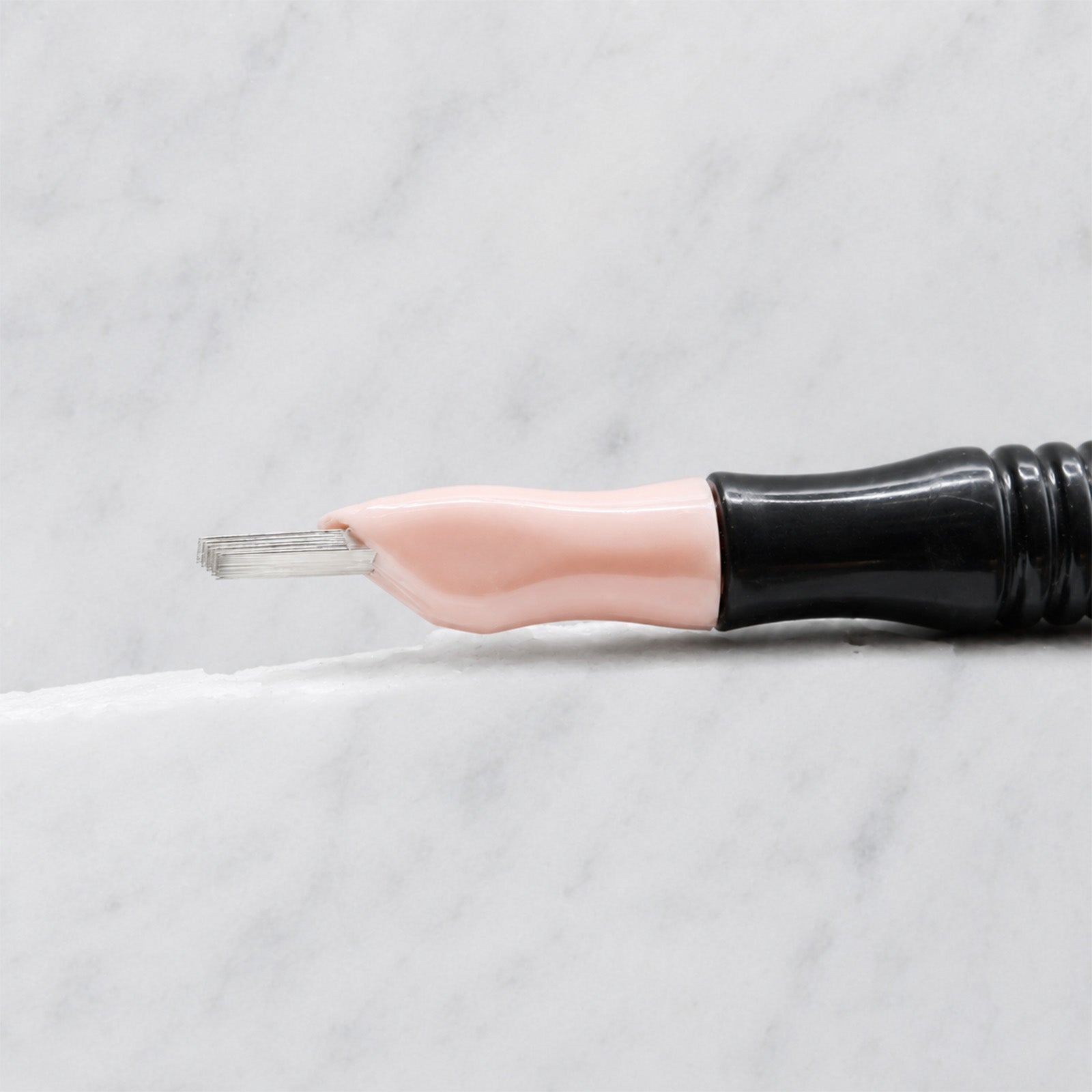 A close-up of SofTap 114 pmu needle click tip, resting on a white marble surface.