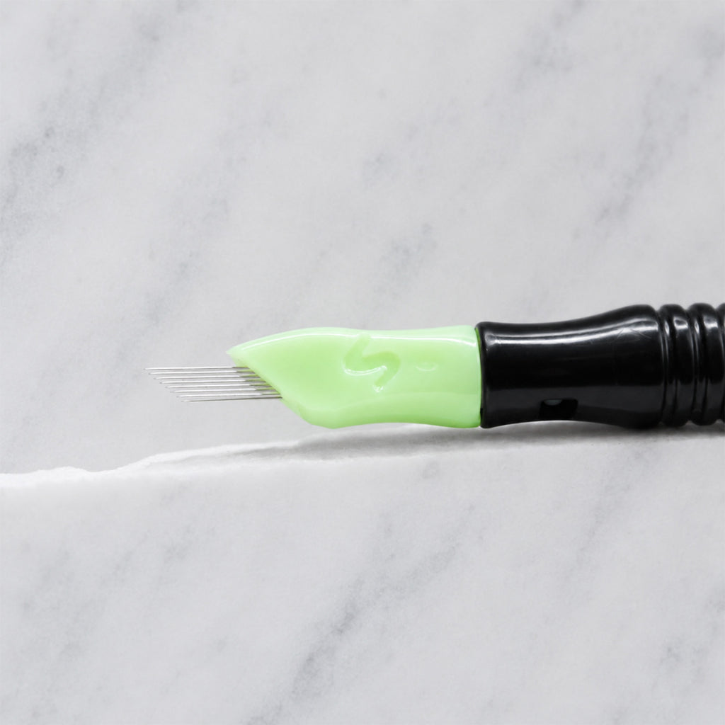 A close-up of SofTap 114 ultimate smudger pmu needle click tip, resting on a white marble surface.