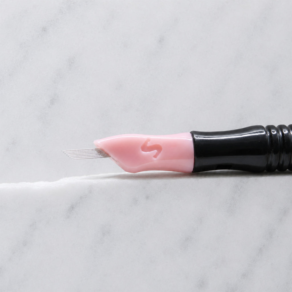 A close-up of SofTap 15 smudger pmu needle click tip, resting on a white marble surface.