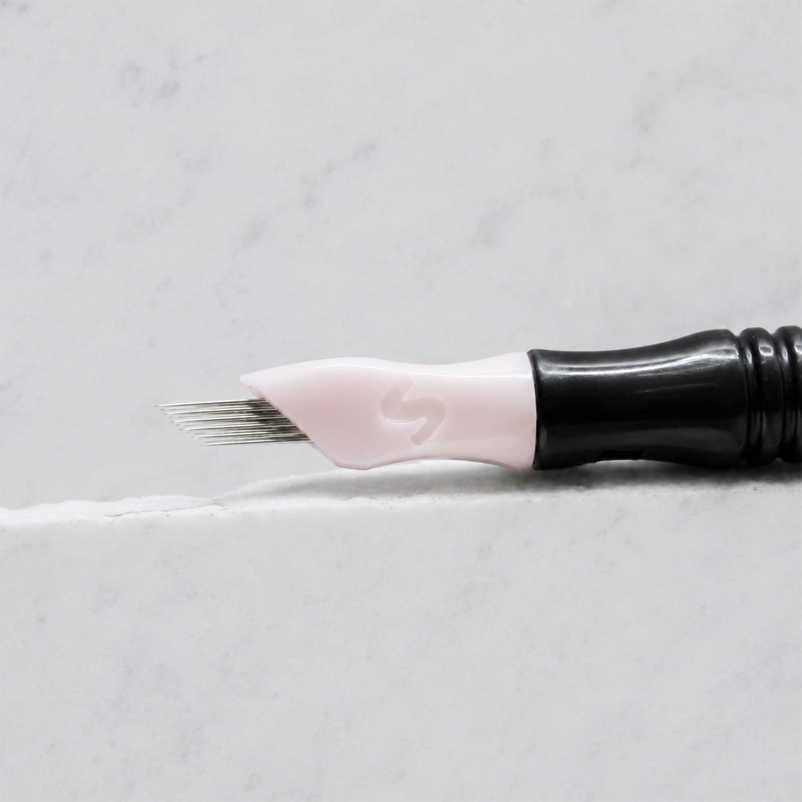 A close-up of SofTap 17 ultimate pmu needle click tip, resting on a white marble surface.