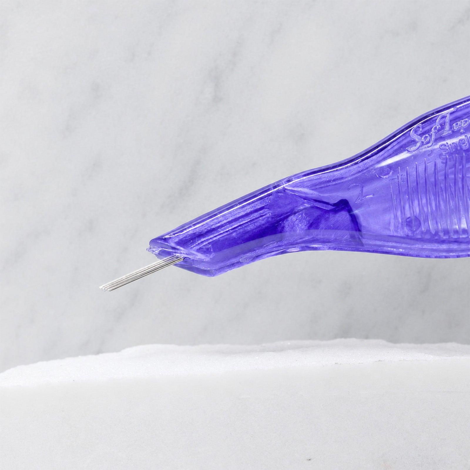 A close-up of SofTap 18 round pmu needle disposable pen, resting on a white marble surface.