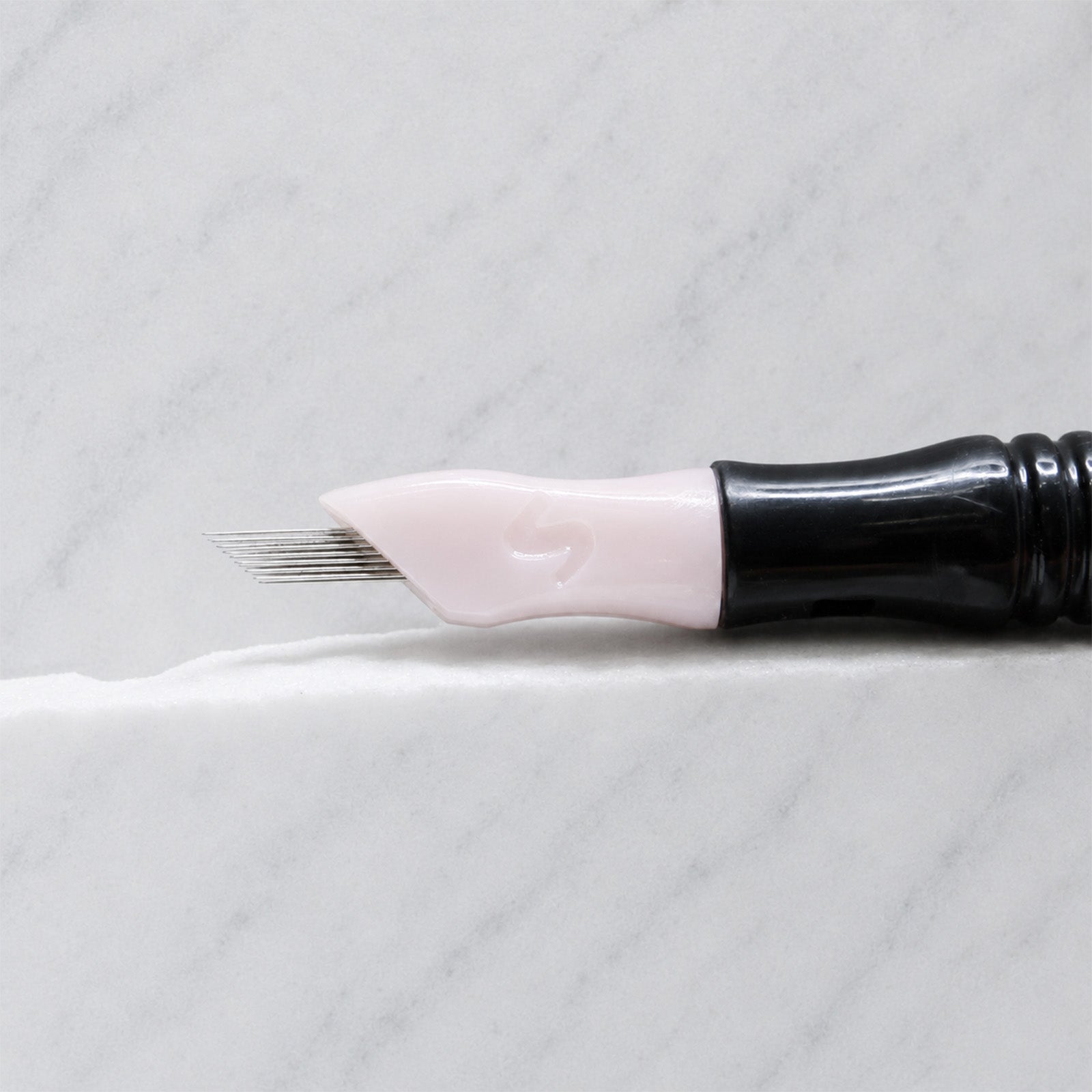 A close-up of SofTap 20 ultimate smudger pmu needle click tip, resting on a white marble surface.