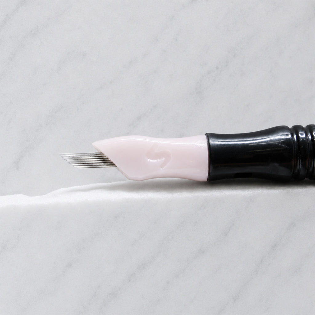 A close-up of SofTap 20 ultimate smudger pmu needle click tip, resting on a white marble surface.