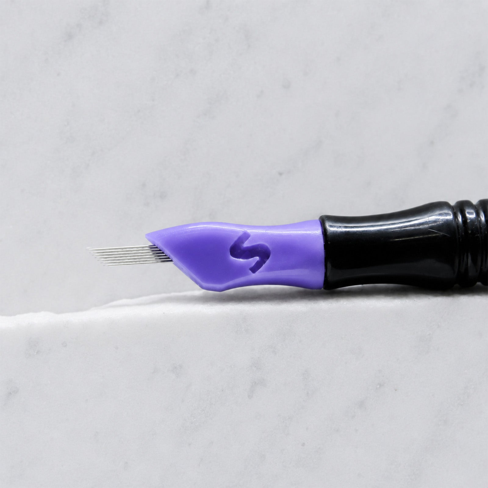 A close-up of SofTap 23 smudger pmu needle click tip, resting on a white marble surface.