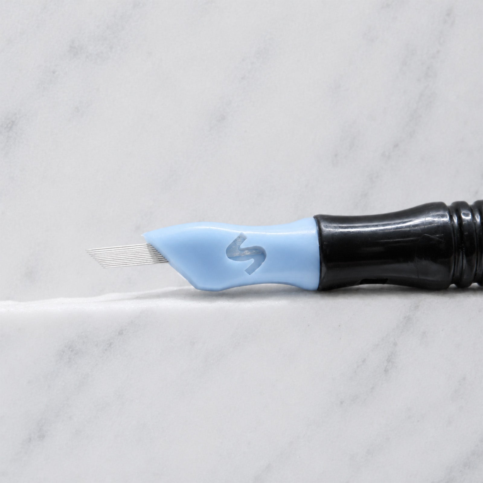 A close-up of SofTap 24 fine pmu needle click tip, resting on a white marble surface.