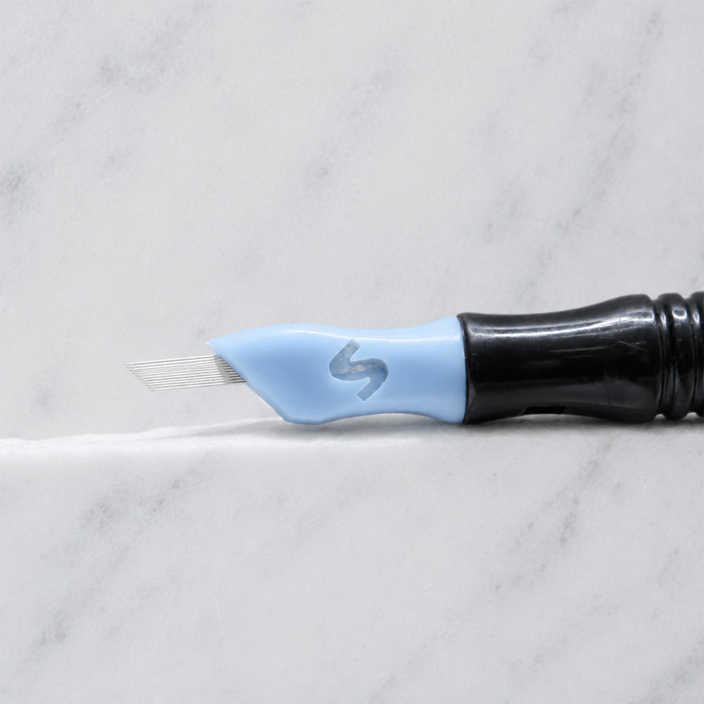 A close-up of SofTap 24 fine pmu needle click tip, resting on a white marble surface.