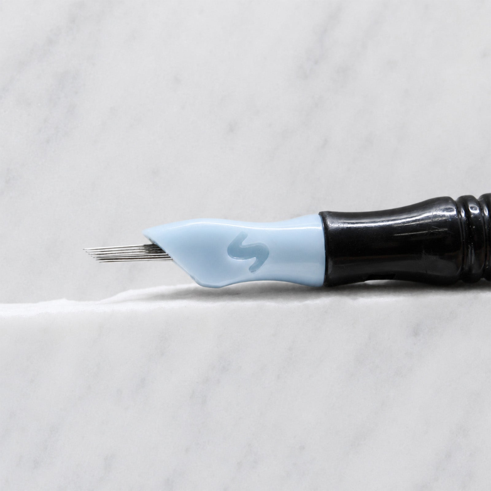 A close-up of SofTap 36 round pmu needle click tip, resting on a white marble surface.