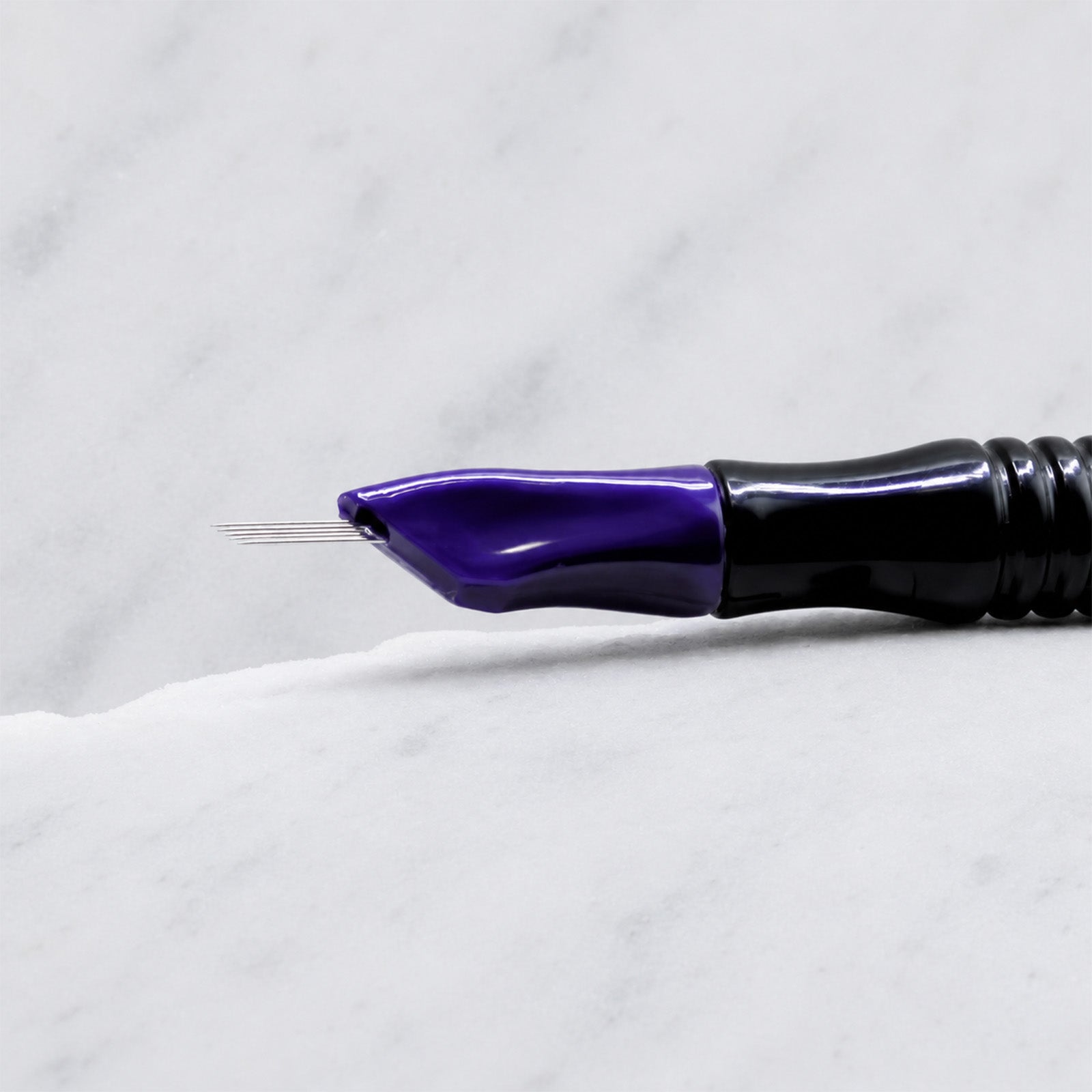 A close-up of SofTap 5 pmu needle click tip, resting on a white marble surface.