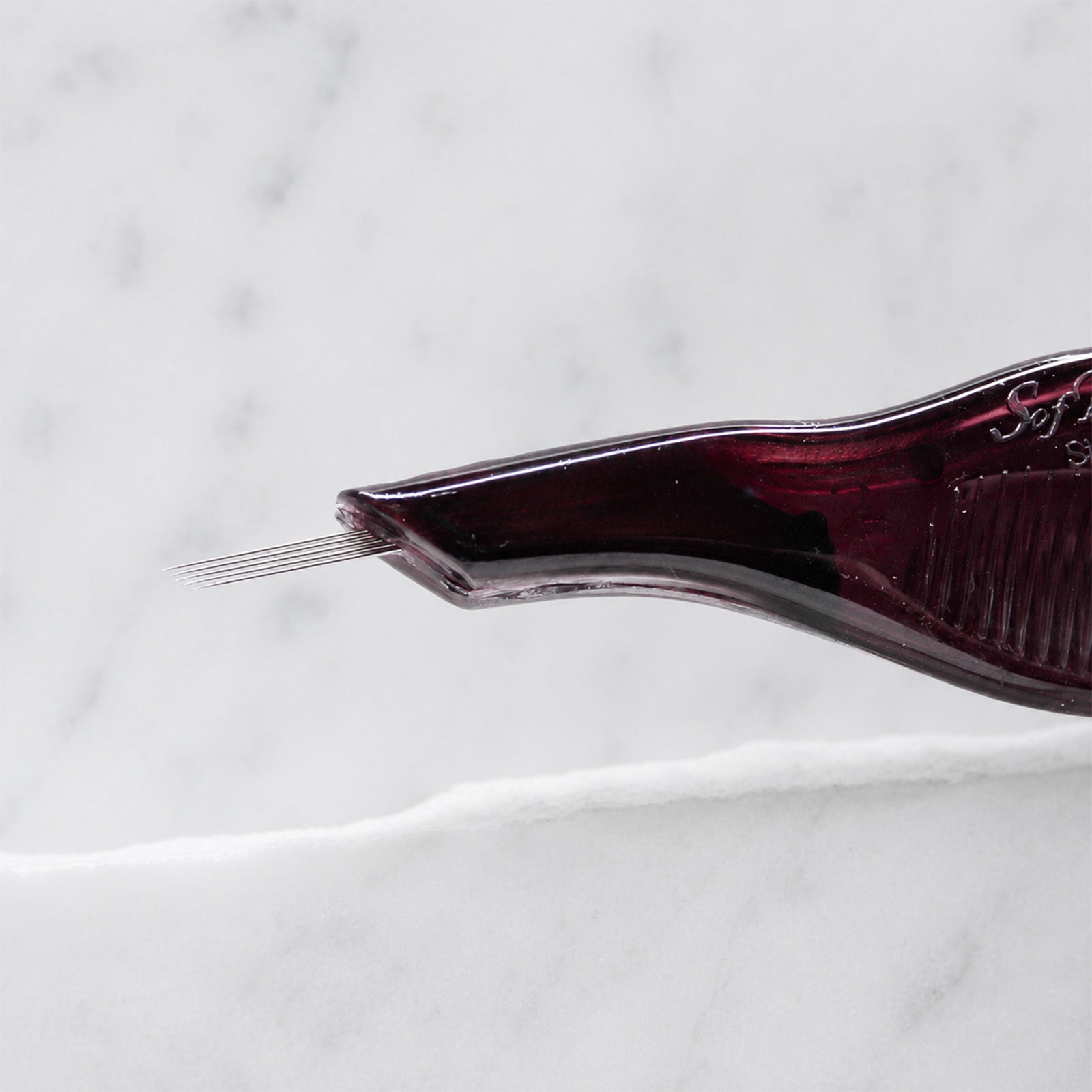 A close-up of SofTap 5 pmu needle disposable pen, resting on a white marble surface.