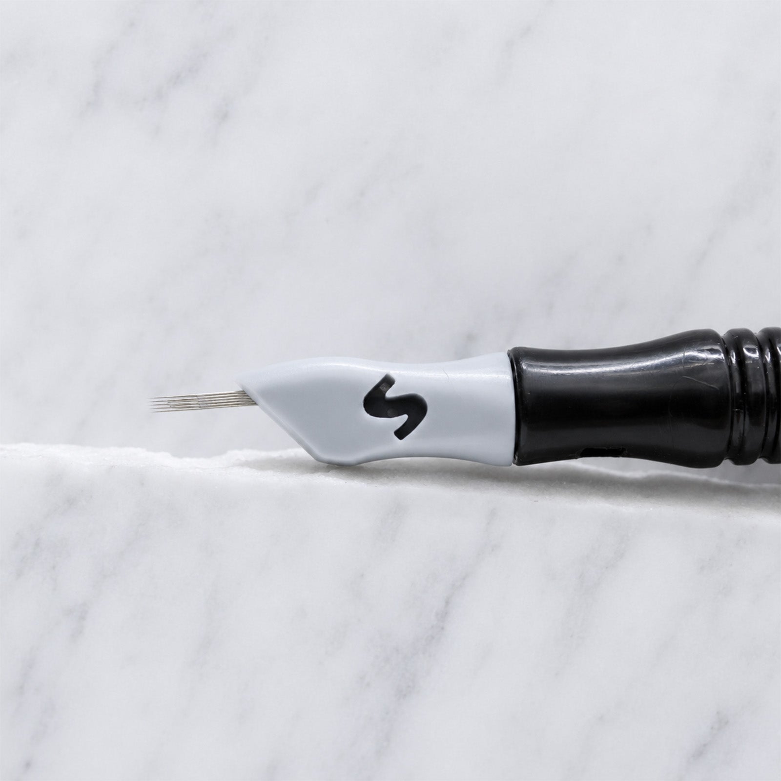 A close-up of SofTap 6 fine curve pmu needle click tip, resting on a white marble surface.