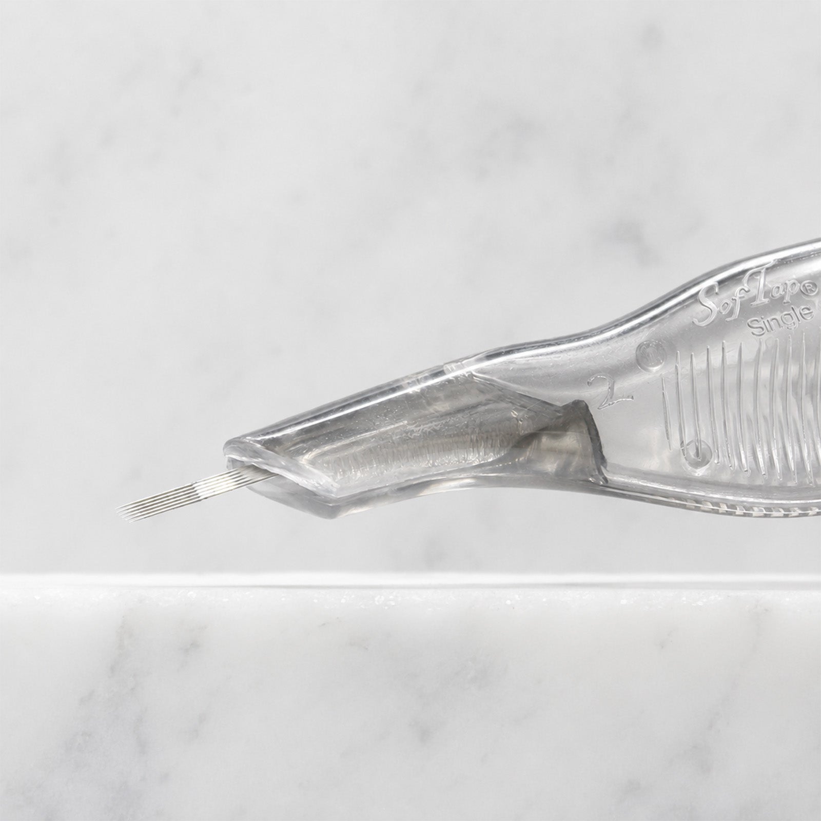 A close-up of SofTap 6 fine curve pmu needle disposable pen, resting on a white marble surface.