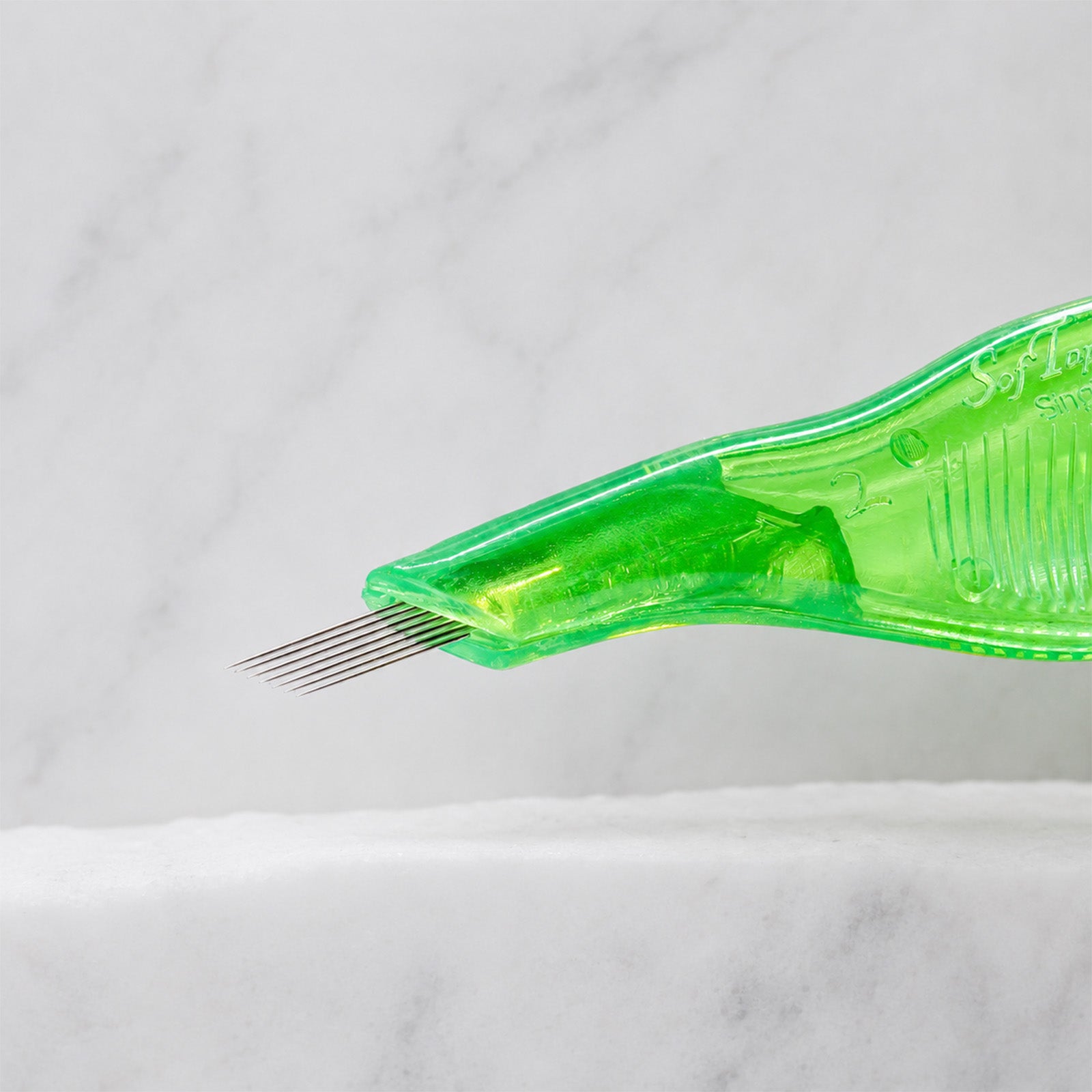 A close-up of SofTap 7 smudger pmu needle disposable pen, resting on a white marble surface.
