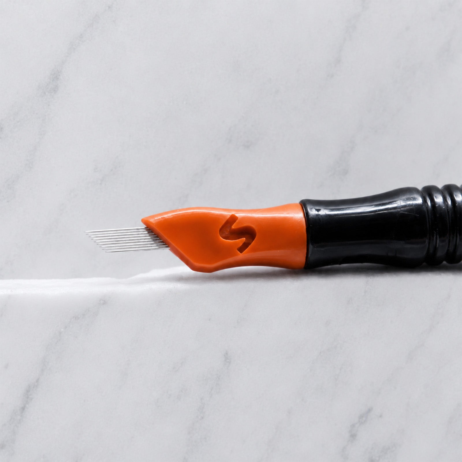 A close-up of SofTap 70 pmu needle click tip, resting on a white marble surface.