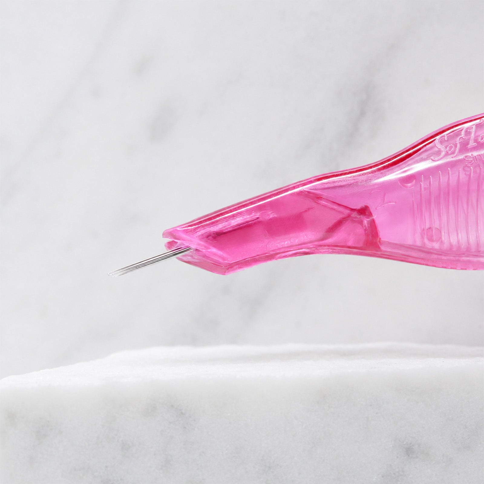 A close-up of SofTap 8 round pmu needle disposable pen, resting on a white marble surface.