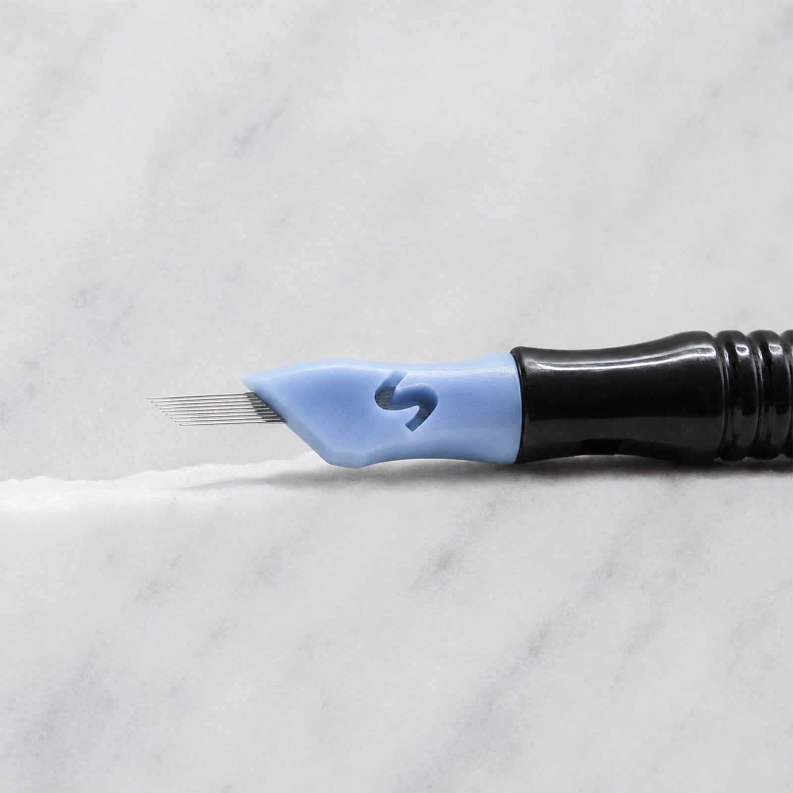 A close-up of SofTap 9 pmu needle click tip, resting on a white marble surface.