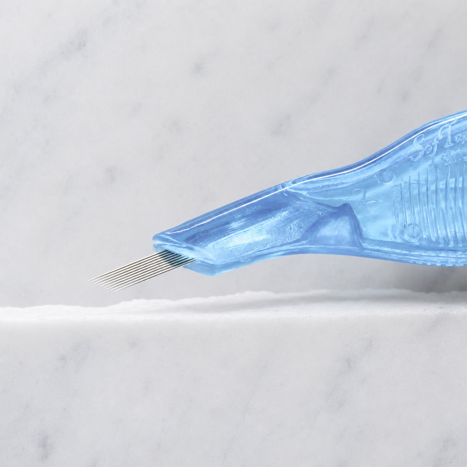 A close-up of SofTap 9 pmu needle disposable pen, resting on a white marble surface.