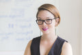 Woman wearing glasses and a black top in front of a whiteboard with text.